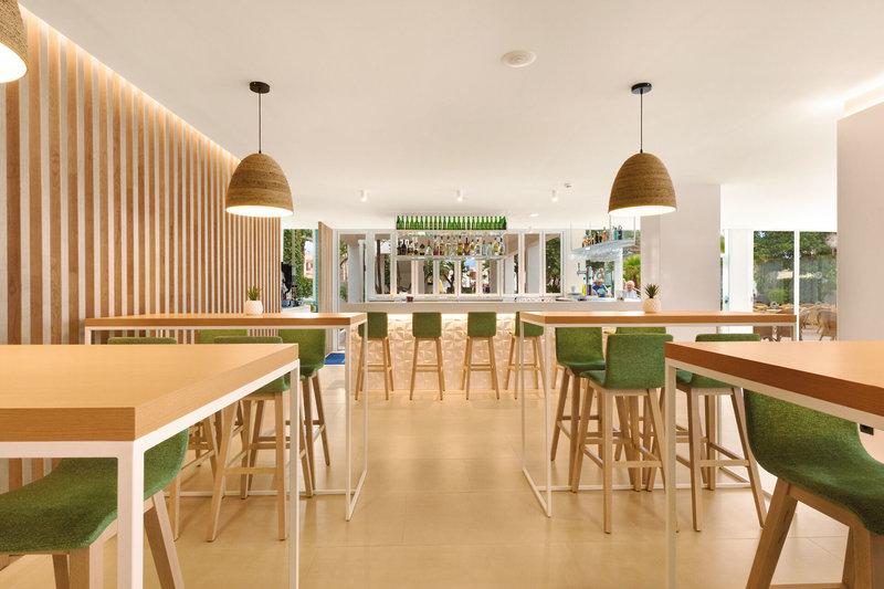 Innenbereich des THB Gran Playa Hotel mit gemusterten Wänden, Holztischen, grünen Stühlen und dekorativen Leuchten.