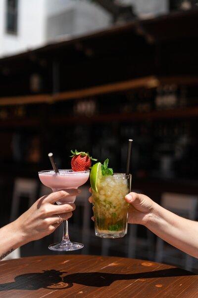Zwei Personen halten Cocktails mit Strohhalmen in einem Hotel.