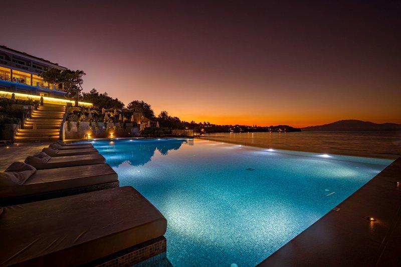 Pool des Alexandra Beach Resorts bei Nacht mit illuminierten Sonnenliegen und Blick auf den Sonnenuntergang