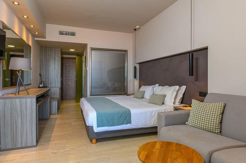 Ein modernes Hotelzimmer im Alexandra Beach Resort mit einem großen Bett, Sofa, Schreibtisch und vielen Fenstern.