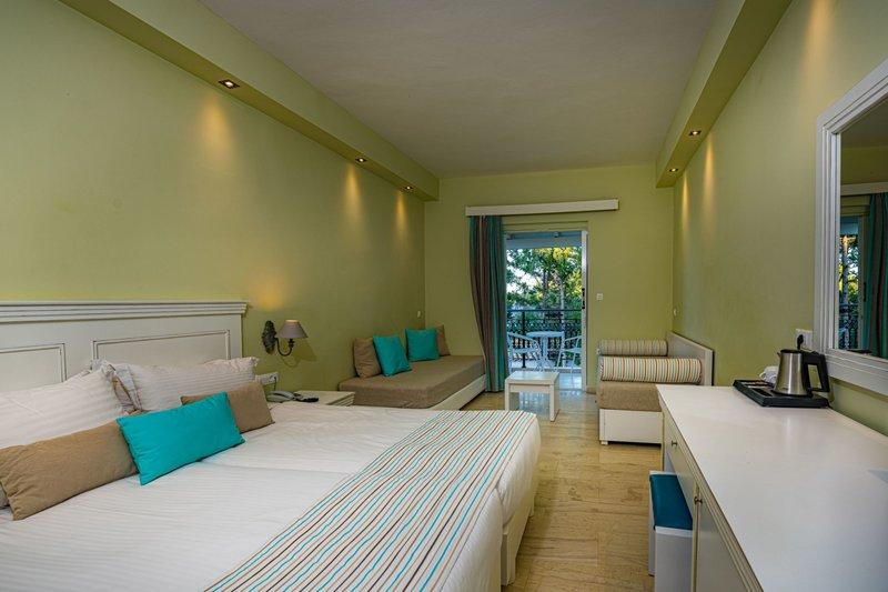 Innenansicht eines Hotelzimmers im Alexandra Beach Resort mit Doppelbett, Sofa und Balkon.