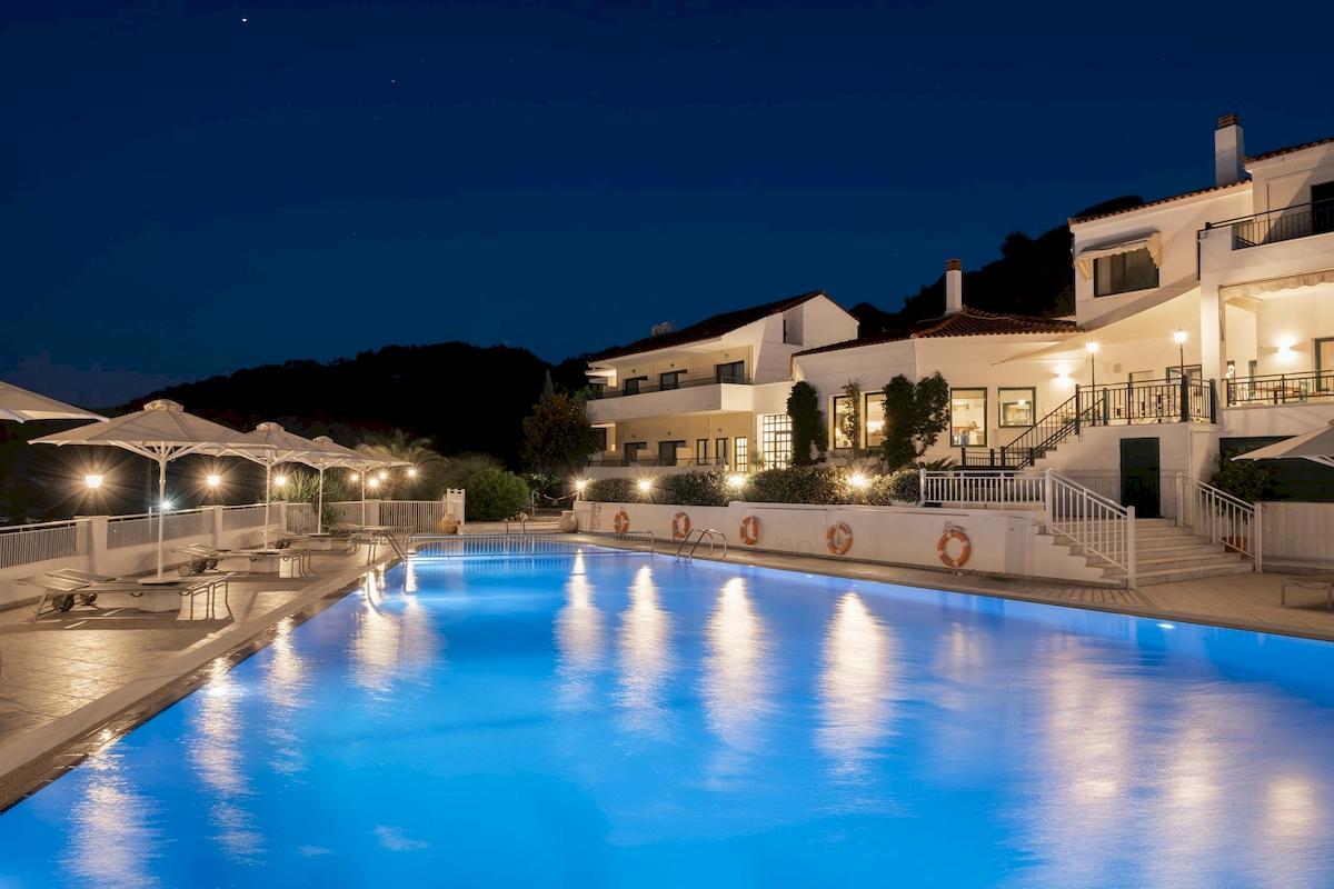 Ein Swimmingpool des Kalidon Panorama Hotels bei Nacht mit leuchtenden Lichtern und blauem Wasser.