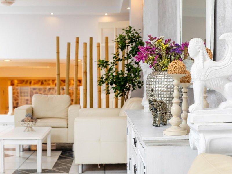 Wohnbereich des Golden Coast Hotels mit weißen Möbeln, einem Blumenvase und Dekorationsartikeln.