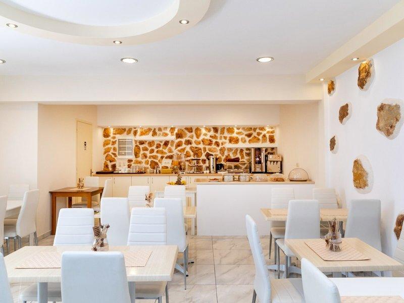 Frühstücksbereich im Golden Coast Hotel mit weißen Möbeln und Steinwand.