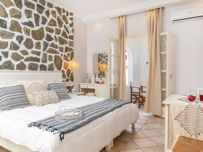 Schlafzimmer im Golden Coast Hotel mit Steinwand, Bett, Nachttisch und offenem Balkon.