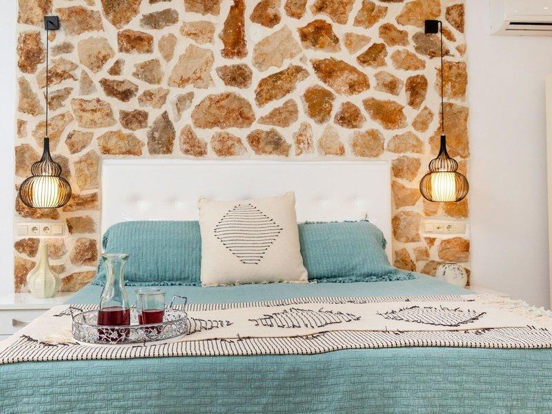 Schlafzimmer mit Steinwand und blauer Bettwäsche, Kissen und Glasflasche auf dem Bett.