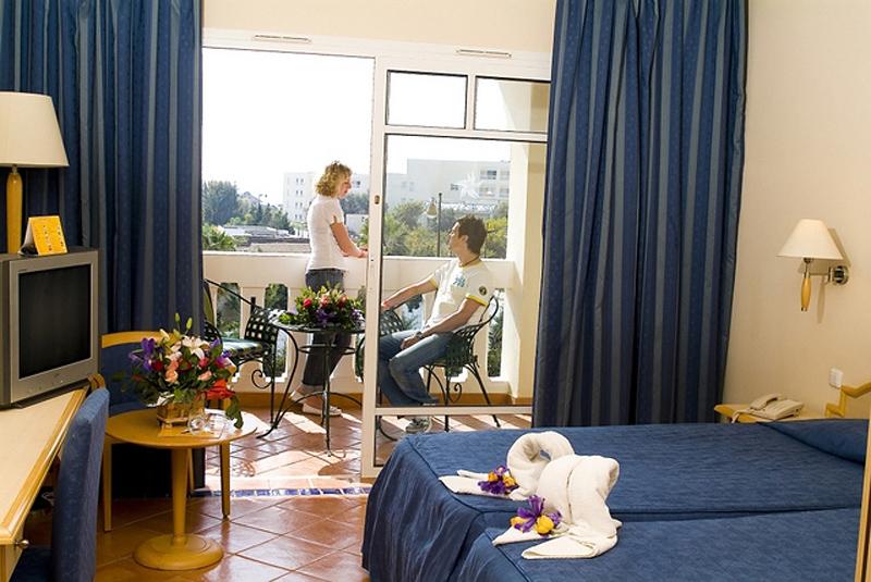 Zimmer mit Balkon im Medina Belisaire & Thalasso Hotel, mit Blick auf eine Frau, die auf den Balkon schaut und einen Mann, der im Stuhl sitzt.