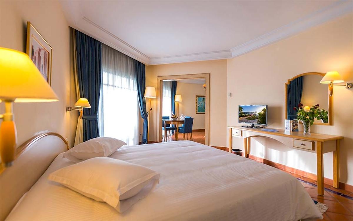Ein modernes Hotelzimmer mit einem großen Bett, Fernseher und einem Schreibtisch im Hintergrund.