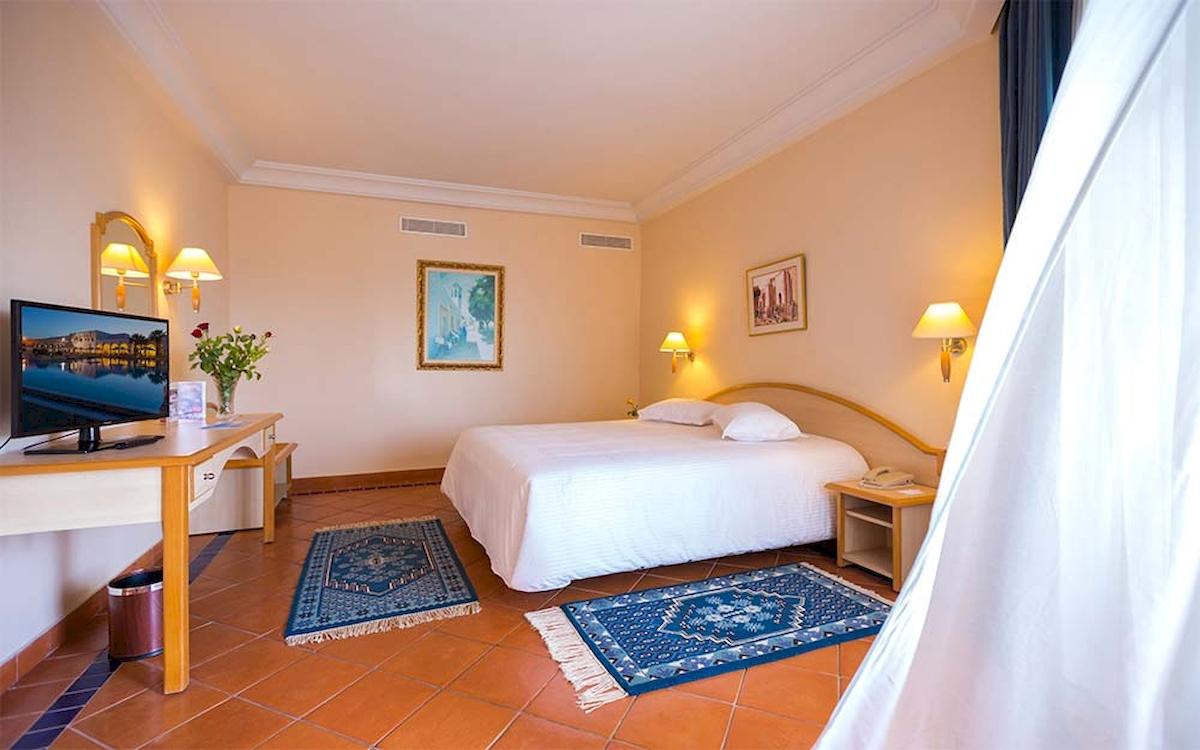 Hotelzimmer im Medina Belisaire & Thalasso mit Bett, Fernseher, Tisch und orientalischen Teppichen.