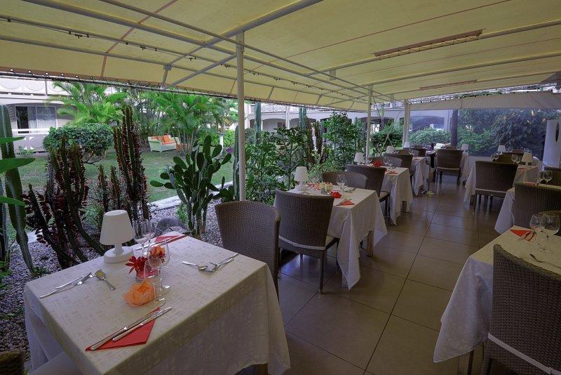 Foto von La Pagerie - Tropical Garden Hotel Restaurant mit Tischen und Stühlen unter einer überdachten Terrasse.