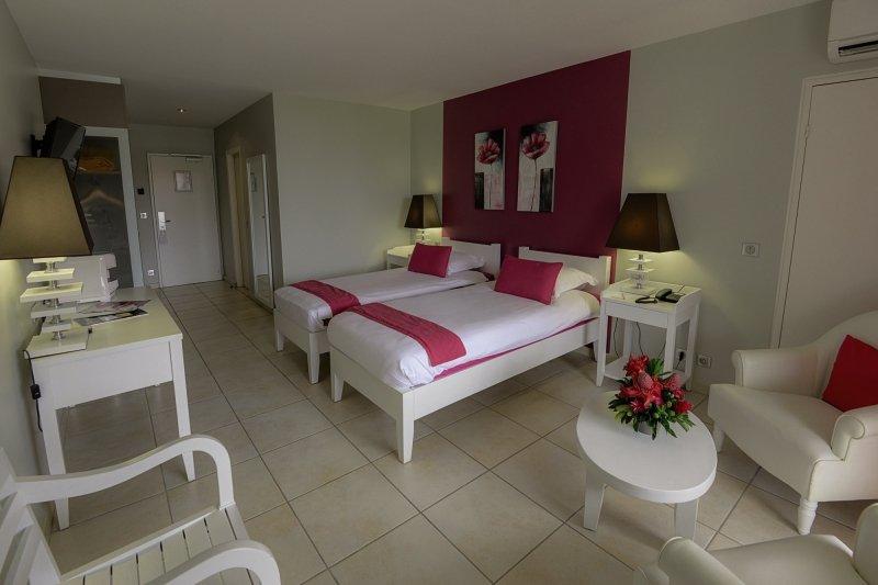 Zwei Betten in einem tropischen Garten Hotel Schlafzimmer mit weißen Möbeln und roten Kissen.