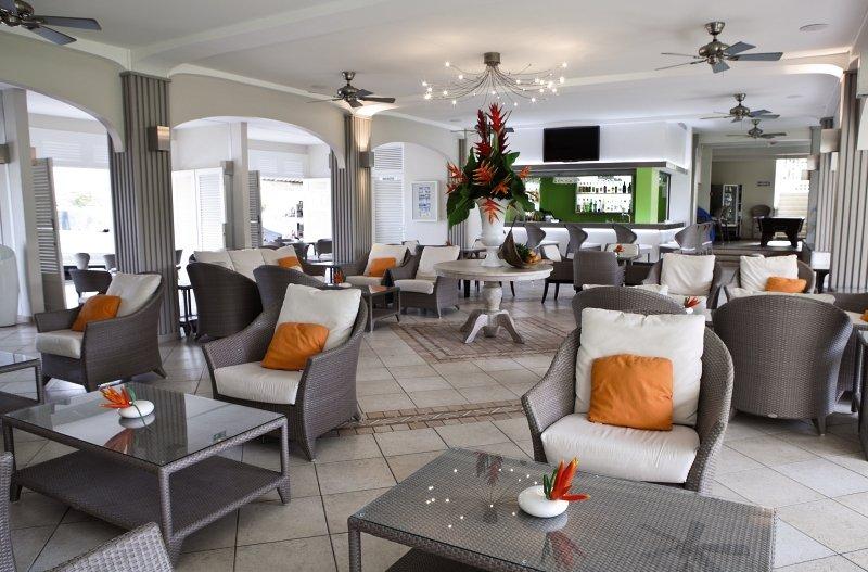 La Pagerie - Tropical Garden Hotel Lounge mit weißen Möbeln und orange Kissen.