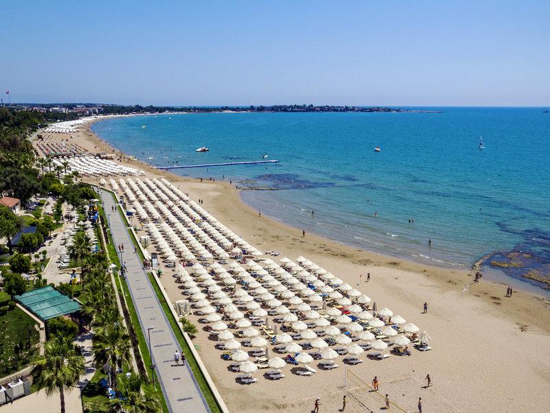 Luftaufnahme des Melas Holiday Village Strandes mit vielen Sonnenschirmen und Besuchern