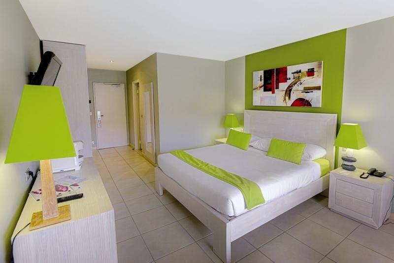 Schlafzimmer im La Pagerie - Tropical Garden Hotel mit grünen Wänden, weißer Bettwäsche und grünen Kissen.