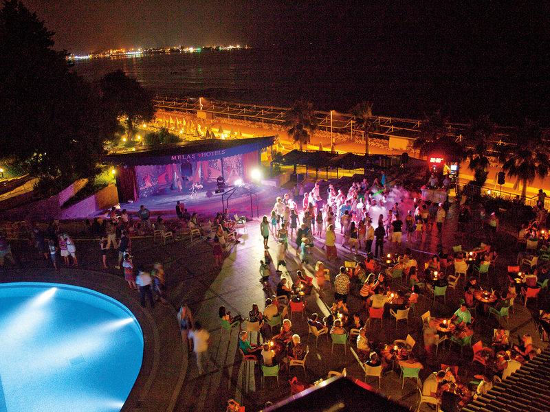 Abendveranstaltung im Melas Holiday Village mit Pool, Bühne und vielen Gästen bei Nacht.