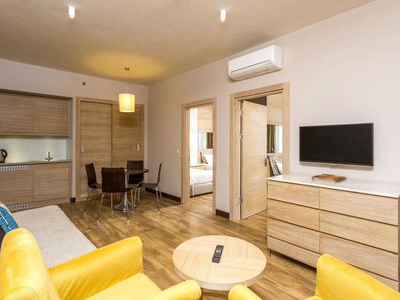 Innenansicht einer Suite im Melas Holiday Village mit Wohnzimmer, Schlafbereich und Küche.