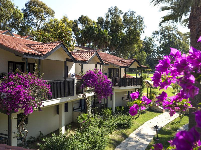Außenansicht der Melas Holiday Village Bungalows mit roten Dächern und blühenden Büschen