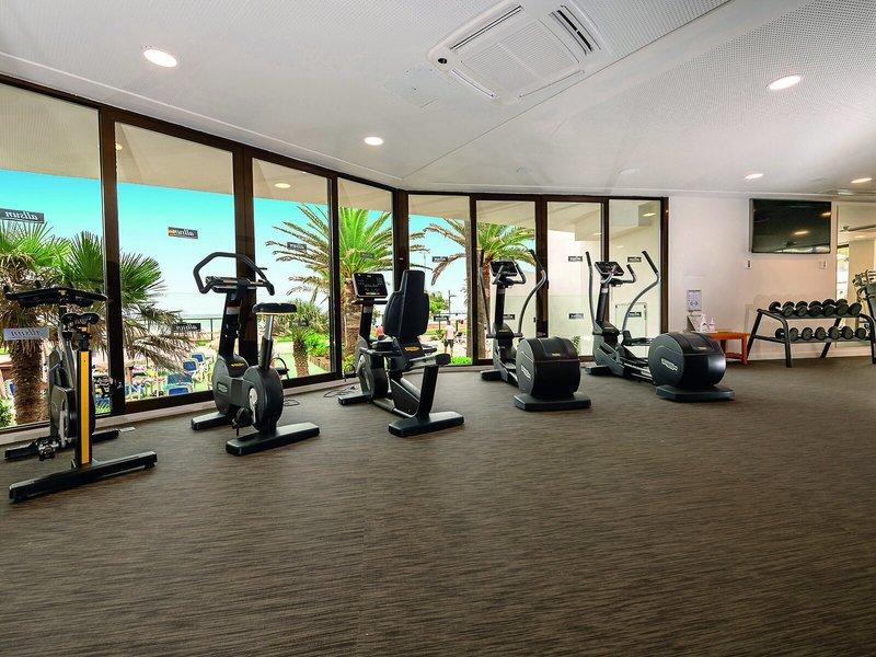 Fitnessstudio im Allsun Hotel Sumba mit Blick auf Palmen und Strand.