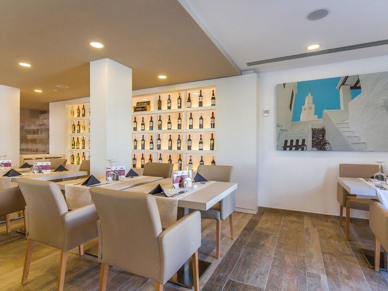 Innenansicht des Restaurants im Marins Playa Suites Hotel mit Tischen, Stühlen und einer Weinflaschenwand.