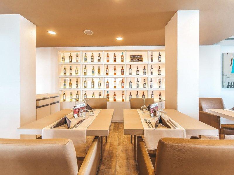 Interieur des Marins Playa Suites Hotels mit geräumigen Esstischen, Holzboden und einer Wand mit Alkoholflaschen.