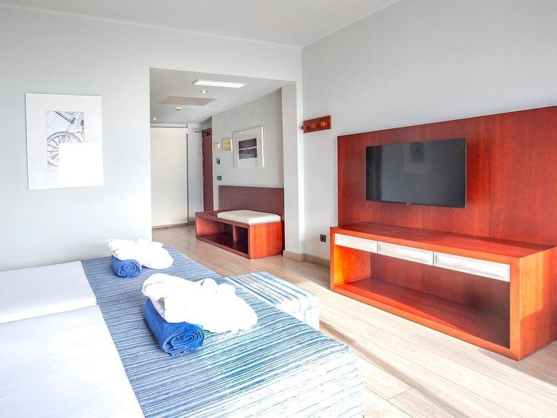 Innenansicht eines Hotelzimmers von Marins Playa Suites mit zwei Betten, Fernseher und Holzmöbeln.