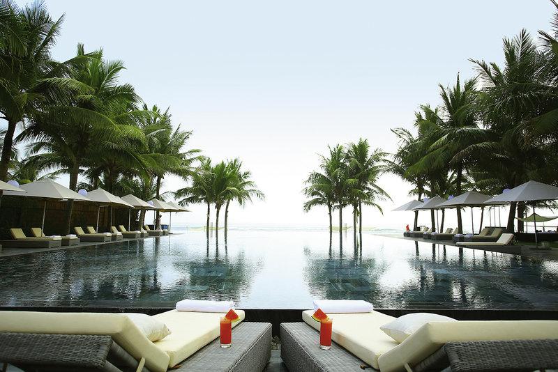 Infinity-Pool des TIA Wellness Resorts mit Liegestühlen und Palmen.
