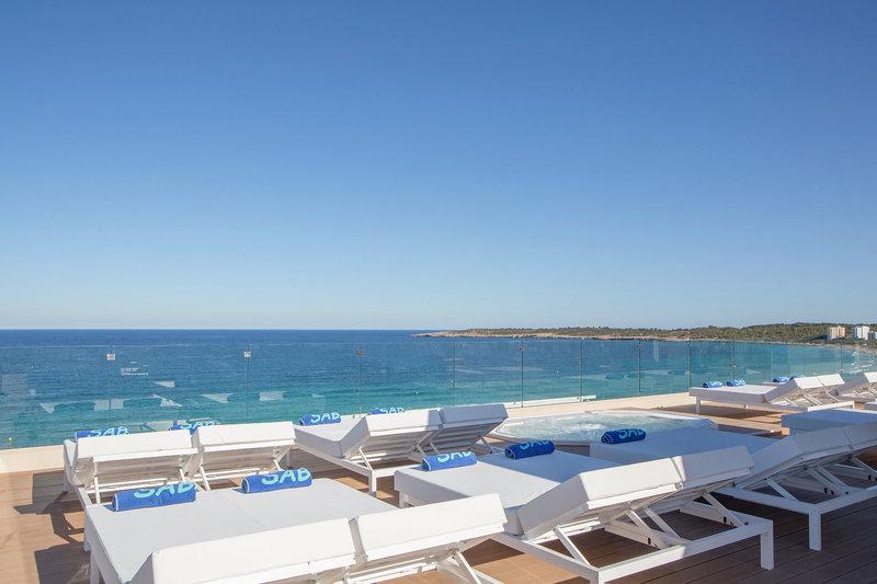 Außenbereich des Sabina & Suites Hotels mit Loungestühlen und Whirlpool, Blick auf das Meer.