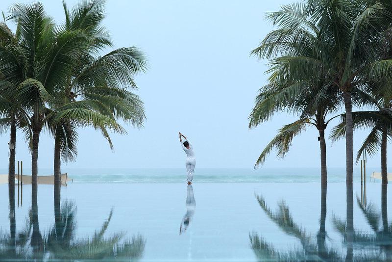 Eine Person macht Yoga auf dem Infinity-Pool des TIA Wellness Resorts am Strand.