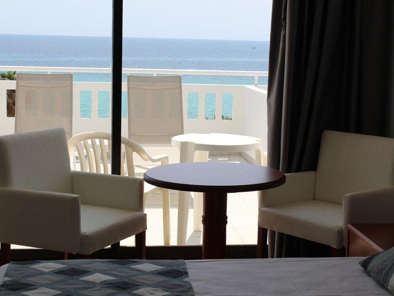 Hotelzimmer mit Meerblick vom Balkon, inklusive Sitzbereich mit Tischen und Stühlen.