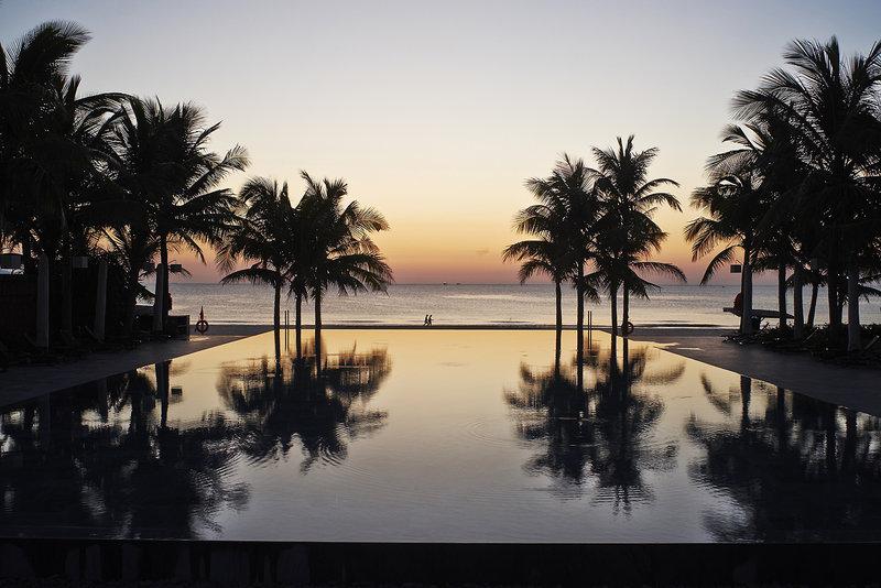 Sonnenuntergang am Strand des TIA Wellness Resorts mit reflektierten Palmen.
