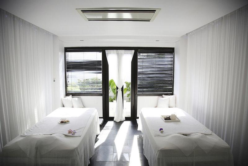 Massageraum im Tia Wellness Resort mit zwei Betten, weißen Laken, Kissen und Vorhängen.