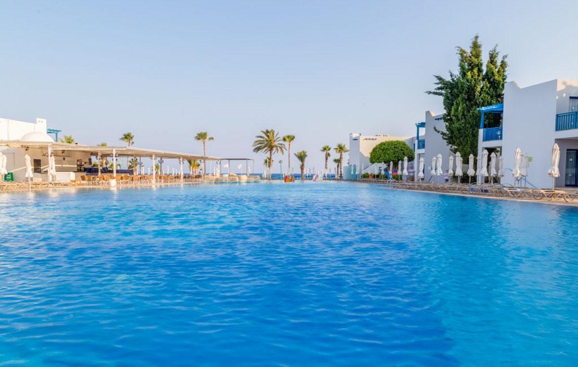 Außenpool des Callisto Holiday Village mit weißen Gebäuden und Sonnenschirmen