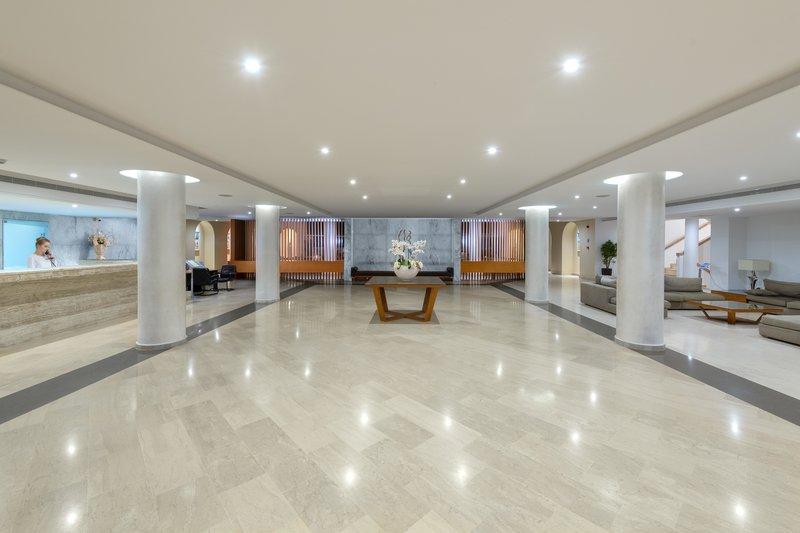 Empfangshalle des Lindos Royal Resorts mit weißem Boden, hohen Säulen und eingeschalteten Deckenleuchten.
