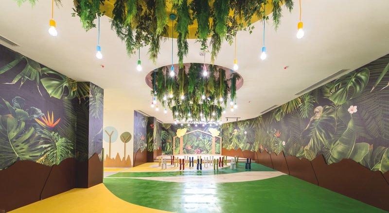 Ein kinderfreundliches Zimmer mit grünen und gelben Böden, bunten Wandmalereien und einer Lichterkrone.