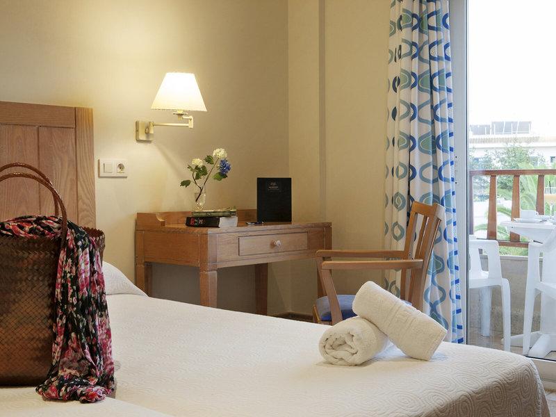 Ein ruhiges Hotelzimmer im Voramar Formentera mit einem Bett, einem Stuhl, einem Tisch und Blick auf den Balkon.