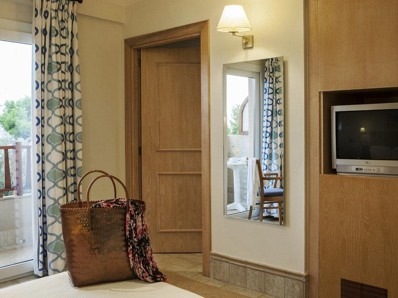 Ein Zimmer im Hotel Voramar Formentera mit einer offenen Tür, einem Spiegel, einem Fernseher und einem Korb auf dem Bett.