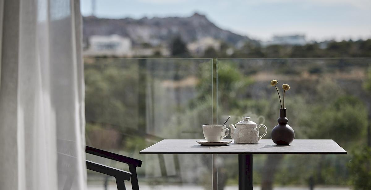 Blick aus einem Zimmer im Helea Lifestyle Beach Resort auf einen Tisch mit Teekanne, Tasse, Untertasse und Vase mit Blumen.