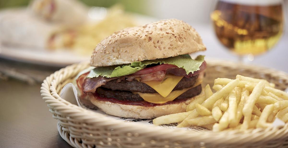 Ein Burger mit Pommes in einem Korb auf einem Tisch neben einem Glas Bier.