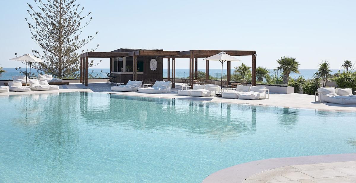 Poolbereich des Helea Lifestyle Beach Resorts mit Blick auf das Meer und weißen Liegestühlen