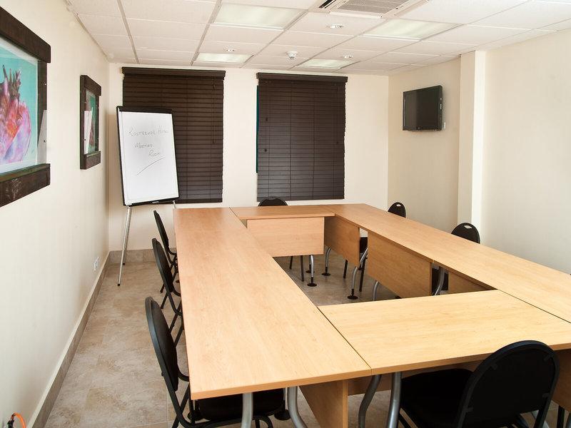 Konferenzraum im Rostrevor Hotel mit langen Holztischen, schwarzen Stühlen, einer Tafel und einer Fernsehwand.