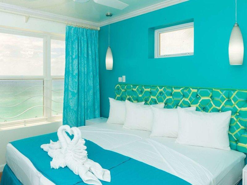 Schlafzimmer im Rostrevor Hotel mit türkisfarbenen Wänden, Blick auf das Meer und ein Bett mit weißen Kissen und türkisen Laken.