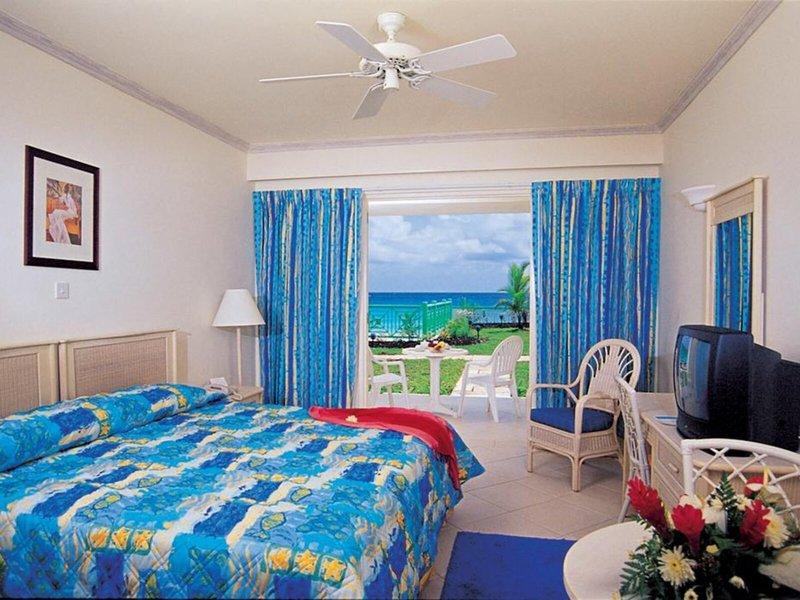 Ein Zimmer im Rostrevor Hotel mit Blick auf das Meer, blauen Vorhängen, einem Bett, einem Fernseher und einem Tisch mit einem Strauß Blumen.
