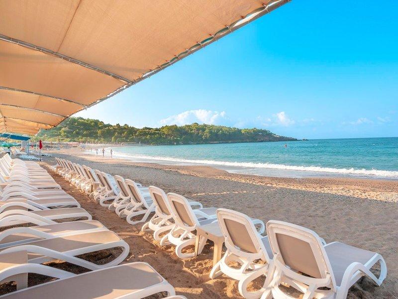 Reihe von weißen Liegestühlen auf dem Strand des Kirman Leodikya Resorts mit Blick auf das Meer.