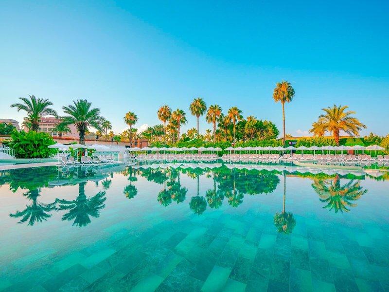 Außenpool des Kirman Leodikya Resorts mit weißen Sonnenliegen und Palmen im Hintergrund