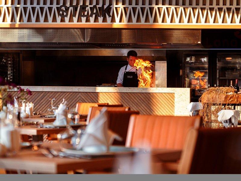 Koch in Steak-Restaurant beim Braten von Steaks mit Feuereffekt in der Küche.