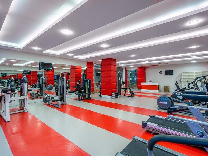Fitnesscenter im Kirman Leodikya Resort mit roten und weißen Bodenstreifen und verschiedenen Fitnessgeräten.