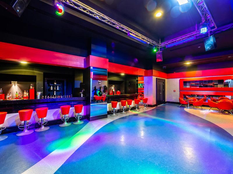 Innenbereich einer Hotelbar mit roten Stühlen, einer Theke und bunten Lichtern