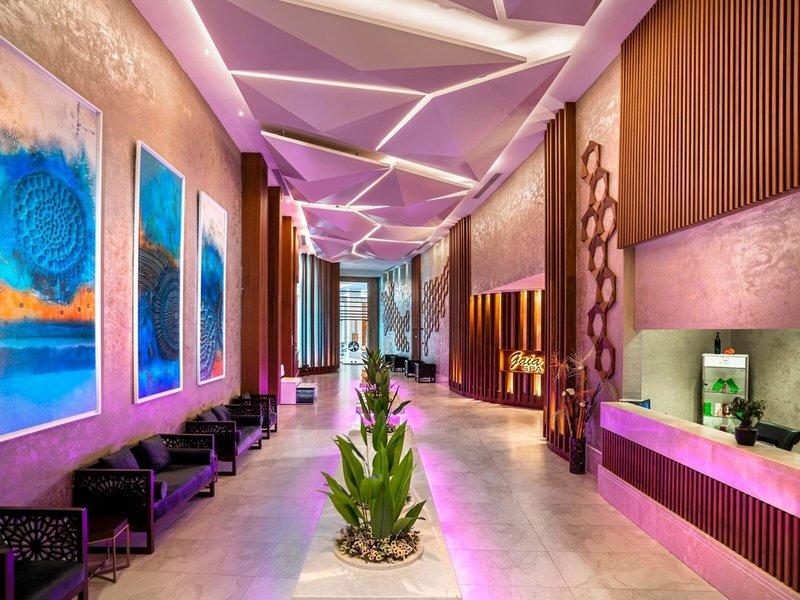 Der Eingangsbereich des Kirman Leodikya Resorts mit gepolsterten Sofas, Gemälden an der Wand, einem Empfangstresen und Pflanzen.