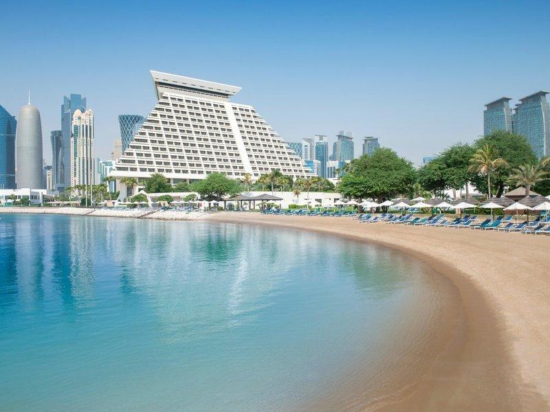 Strand vor dem Sheraton Doha Resort Convention Hotel mit blauem Wasser und vielen Liegen
