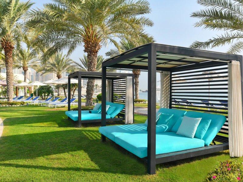 Außenbereich des Sheraton Doha Resort Convention Hotels mit blauen Loungesofas auf Rasen.